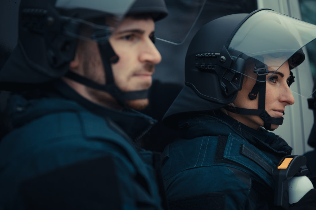 Zu sehen sind zwei Polizisten in voller Schutzausstattung. Sie tragen einen Einsatzhelm der Firma Buschprotective. Sie schauen beide an der Kamera vorbei.