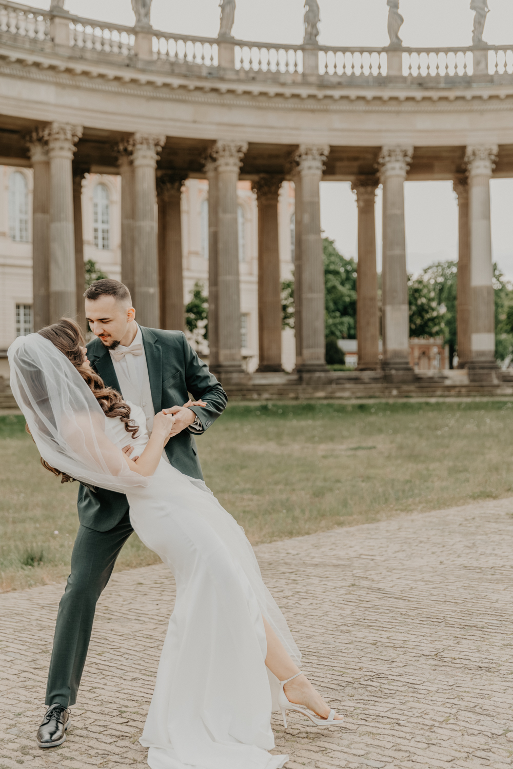 Das Brautpaar tanzt vor einem großen Bogen am Neuen Palais in Potsdam. Der Bräutigam hält seine Frau Fest. Das ganze gehört zu einer ganztätigen Hochzeitsreportage.